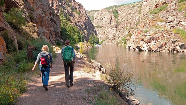 A photo of two people hiking on a path along a waterway